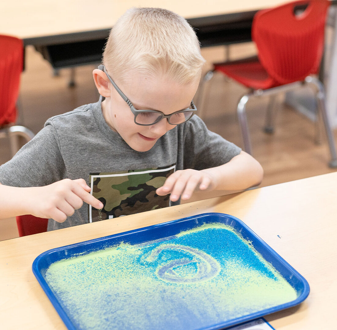 IMSE student using a sand tray for letter formation